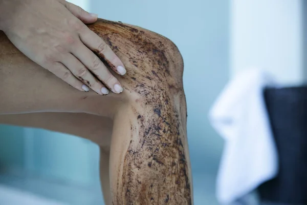 DIY Coffee scrub. Beauty skin care. Young woman putting coffee scrub on her legs.