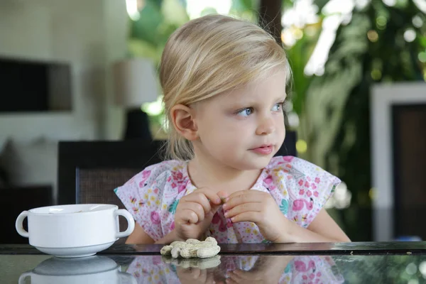 Toddler girl eating peanuts in shell on the kitchen table