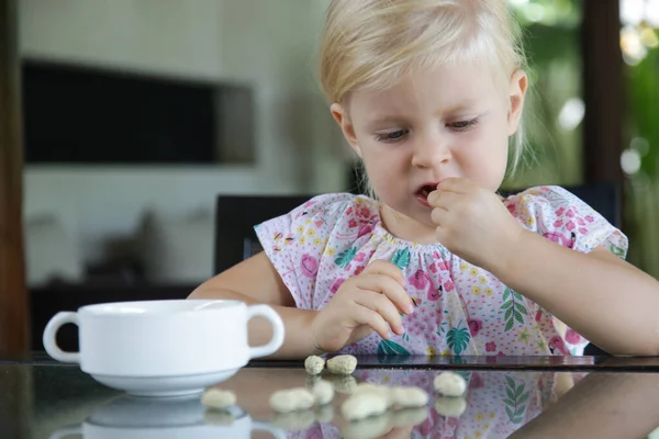 Toddler girl eating peanuts in shell on the kitchen table