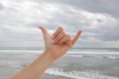 El sıkışma hareketi. Uzatılmış başparmak ve serçe parmağıyla mavi gökyüzüne ve okyanusa uzanan gevşek bir yumruk..