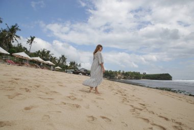 Kumsalda duran ve ufka bakan bir kadın. Kasvetli yaz gününde sahilde uzun beyaz elbiseli bir kadın.. 