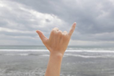El sıkışma hareketi. Uzatılmış başparmak ve serçe parmağıyla mavi gökyüzüne ve okyanusa uzanan gevşek bir yumruk..