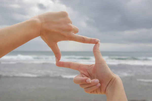 青い海の地平線の前にフレームの形をした手を持つ女性 — ストック写真