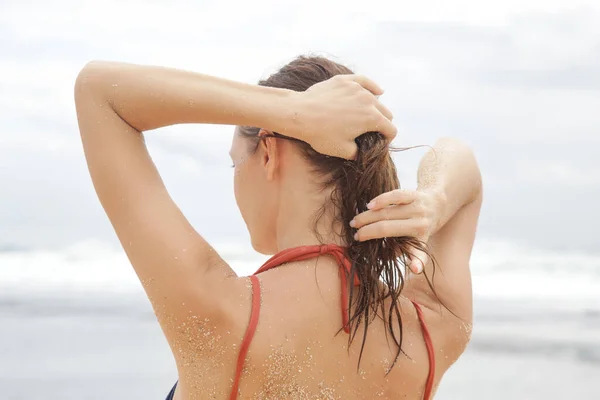Young brunette applying hair oil on the beach, summertime hair care concept.