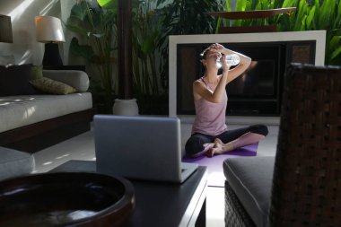 Evde günlük yoga rutininden sonra su içen genç bir kadın. Sağlıklı yaşam tarzı kavramı.