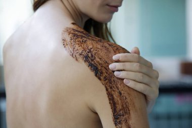 Kahve fırçası. Güzel cilt bakımı. Genç bir kadın omuzlarına ve boynuna kahve fırçası sürüyor..