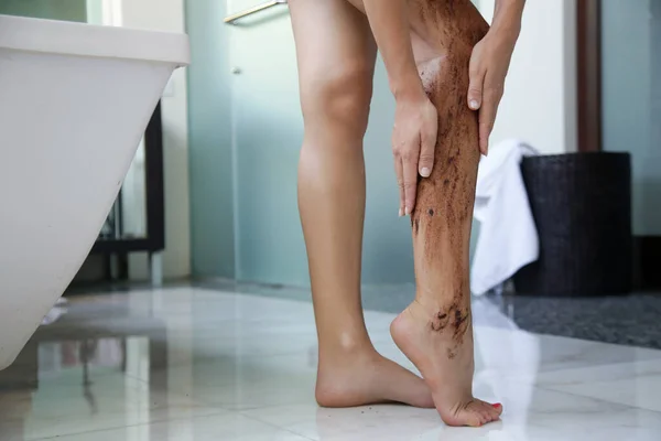 DIY Coffee scrub. Beauty skin care. Young woman putting coffee scrub on her legs.