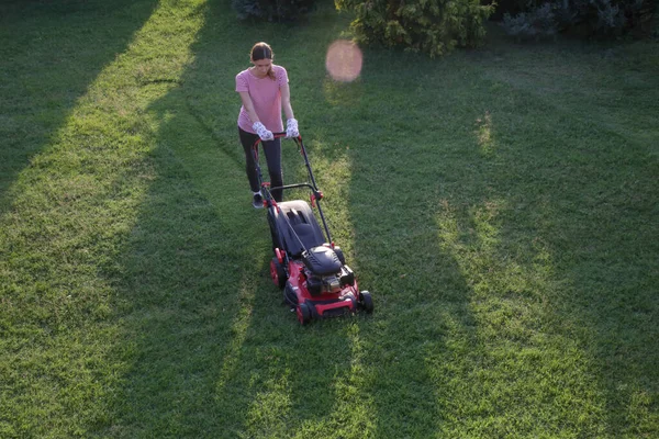 芝生の芝刈り機で草を切る若い女性 屋外家事コンセプト — ストック写真