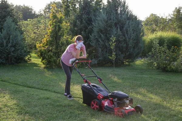 芝生の芝刈り機で草を切りながら短い休憩をする疲れた女性 屋外家事コンセプト — ストック写真