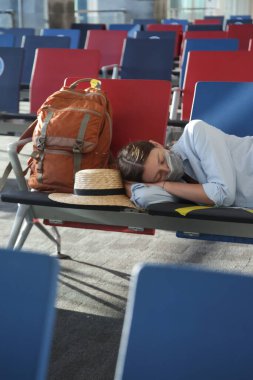 Koruyucu tıbbi maskeli yorgun turist kadın uçuş için beklerken terminalin kapısında uyuyor. Kaçırılmış uçuş, uçuş gecikmesi ya da iptal konsepti. Coronavirüs salgını sırasında seyahat etmek.