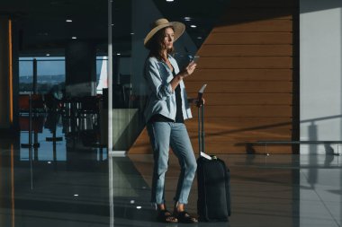 Şapkalı ve el bagajlı bir turist havaalanında bekliyor..