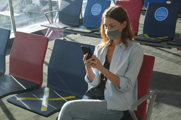 stock image Tourist woman traveling with mask and using phone at the airport. Safety measures during coronavirus. New normal concept.