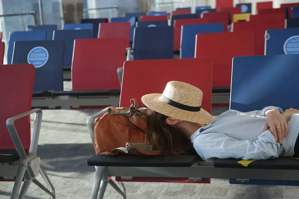 Tired tourist woman sleeping on the seats in the waiting area while waiting for the fligh at the empty airport. Missed flight, flight delay or cancelation concept.