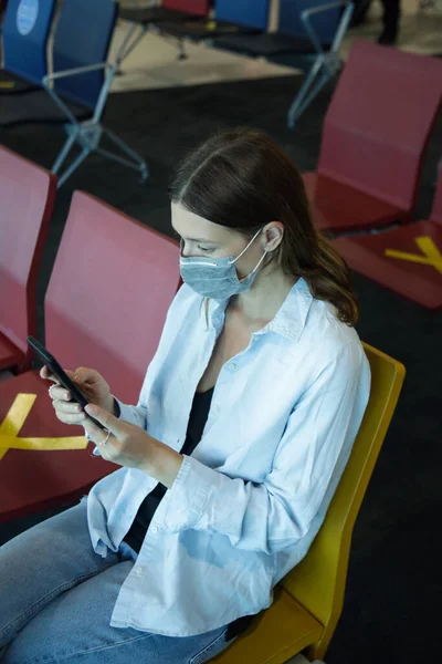 Tourist woman traveling with mask and using phone at the airport. Safety measures during coronavirus. New normal concept.