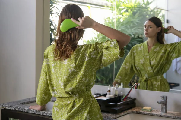 ヘアケア 鏡の前のバスルームでプラスチック製のデタングリング髪ブラシと髪をもたらすブルネットの女性のまれなビュー — ストック写真