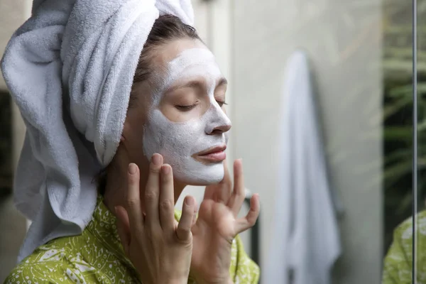 浴室の若い女性の顔のマスクでタオルで包まれた ホームスパとスキンケアのコンセプト — ストック写真