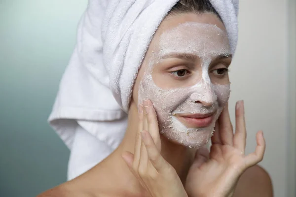 浴室の若い女性の顔のマスクでタオルで包まれた ホームスパとスキンケアのコンセプト — ストック写真