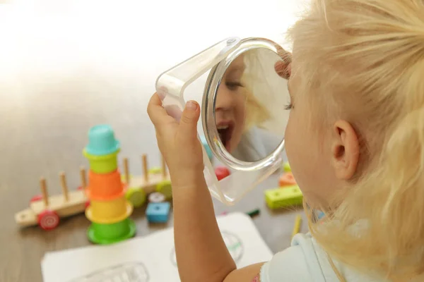 Little toddler girl holding a mirror and making facial expression