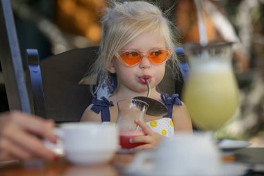 Modaya uygun. 3 yaşında bir kız yeniden kullanılabilir metal pipetle meyve suyu içiyor.