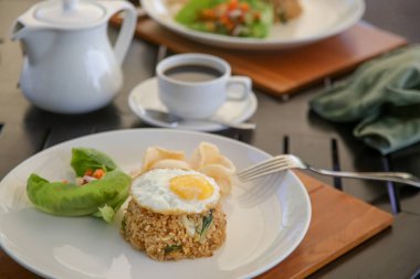 Kızarmış pirinç, kızarmış yumurta ve bir fincan kahve ile servis edilir.