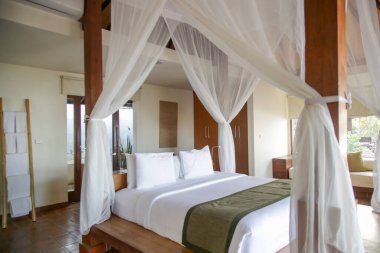 Büyük boy yatak, sivrisinek ağlı, yatak odasının içi beyaz renklerde, insan yok.