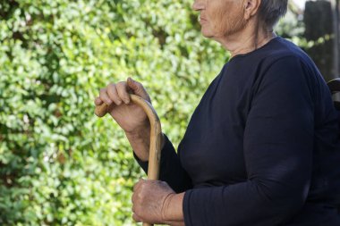 Yaşlı kadın parkta tahta baston tutuyor.