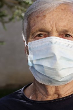 Koruyucu tıbbi maske takan yaşlı beyaz kadın portresi. Koronavirüs salgını sırasında güvenlik önlemleri.