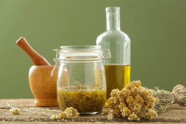 Herbal infused oil with ingredients. Yellow immortelle flowers, cold pressed olive oil, mortar and pestle. Process of maceration. clipart