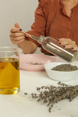 Kadın lavanta çiçekleriyle bitkisel yağ yapıyor. Doğal organik ev yapımı kozmetik ürünlerinin erimesi. Fotoğraf serisi.