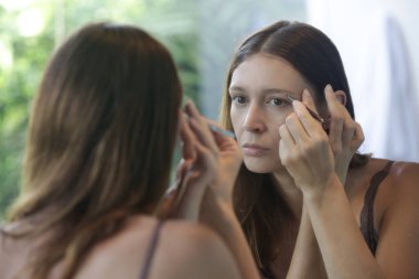 Genç beyaz kadın aynanın önünde kaşlarını yoluyor..