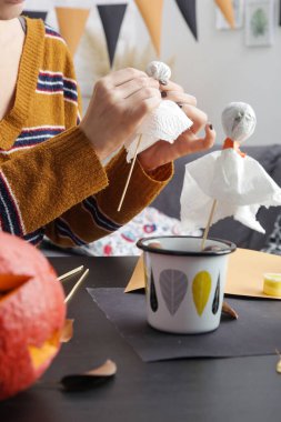 Evde cadılar bayramı süsleri yapan genç bir kadın. Sonbahar sezonu DIY zanaatı. Kadın sopayla kağıt hayalet yapıyor, bir sürü fotoğraf..