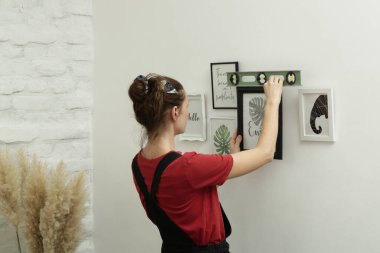 Yeni evin duvarlarında resim çerçeveleri düzenleyen kadın, ev geliştirme konseptini bozuyor.