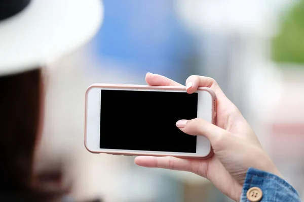 Mujer mano usando teléfono inteligente con pantalla en blanco sobre fondo borroso — Foto de Stock