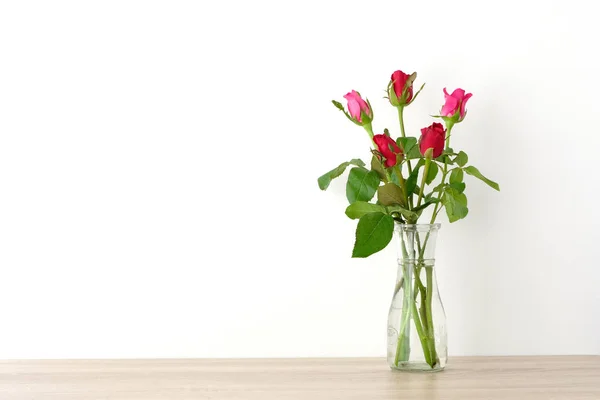 Rosas vermelhas e rosa em vaso de vidro na mesa e backgro parede branca — Fotografia de Stock