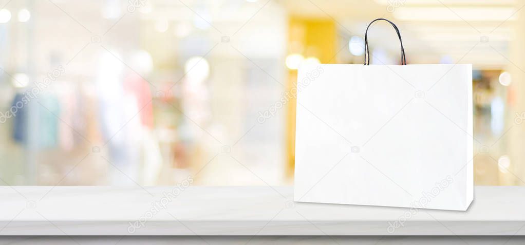 White paper shopping bag standing on white marble  table over bl