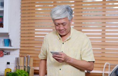 Mutfakta dururken akıllı telefon kullanan üst düzey Asyalı adam 