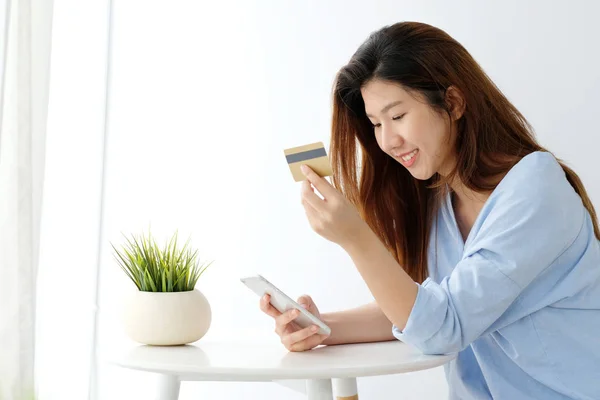 Genç Asyalı kadın kredi kartı tutan ve akıllı telefon kullanarak 