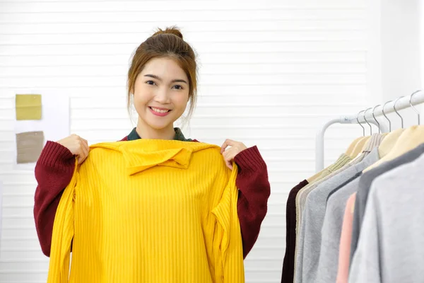 Joven mujer asiática diseñador de moda mostrando amarillo suéter mientras —  Fotos de Stock