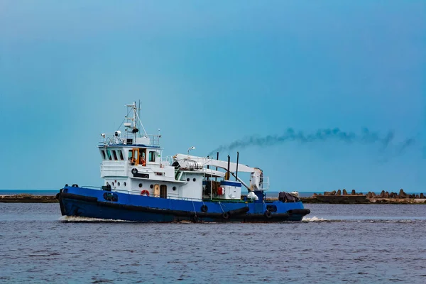 Blue tug ship moving to the cargo terminal. Industrial services