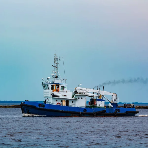 Blue tug ship moving to the cargo terminal. Industrial services