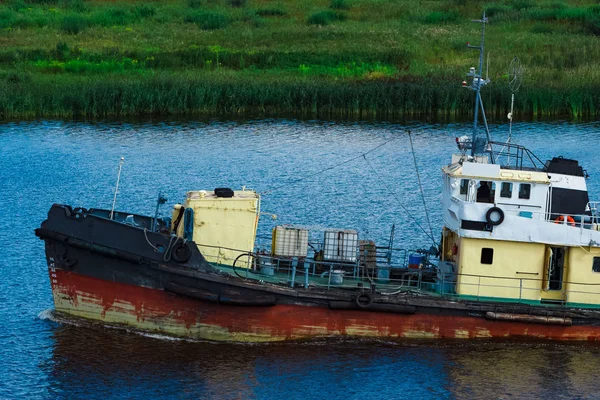 Old tug ship moving to the cargo terminal. Industrial service