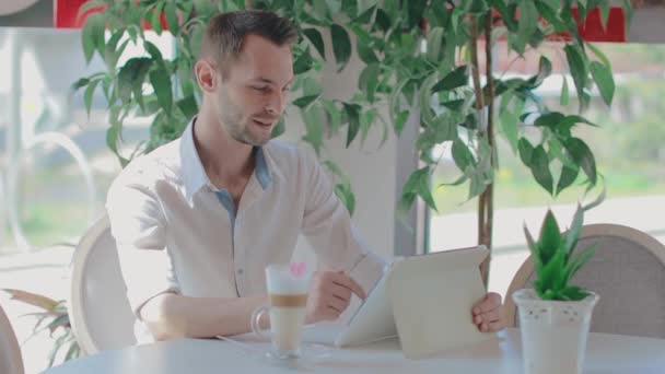 Cliente jovem faz chamada de vídeo em um café usando Tablet PC — Vídeo de Stock