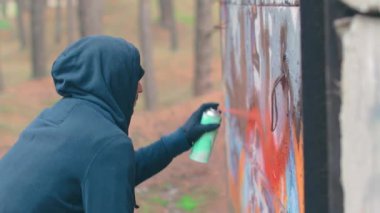 Grafiti çizen genç adam sprey boya kutusu kullanıyor.