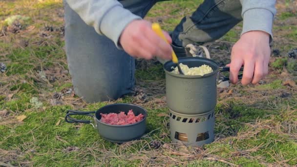 Wandelaar is Pasta koken met blikken stoofpot in een bos — Stockvideo