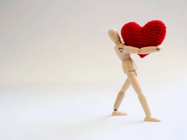 Wooden puppet standing and holding a red heart on the white screen background. Wooden puppet holding the heart with love and care.
