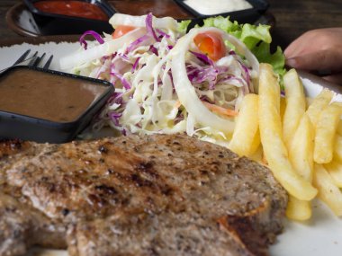 T-bone Steak tuz ve biber, altın kızarmış patates ve yeşil sebzeler ile kapatın. Beyaz tabak, çatal ve bıçak, restoranda ahşap masa