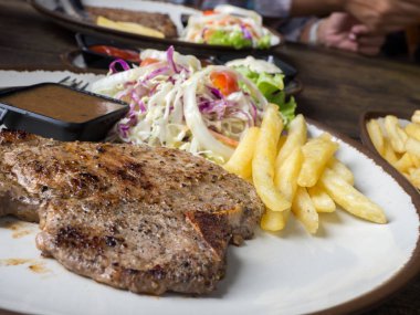 T-bone Steak tuz ve biber, altın kızarmış patates ve yeşil sebzeler ile kapatın. Beyaz tabak, çatal ve bıçak, restoranda ahşap masa