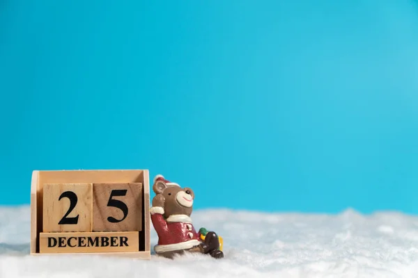 Brown bear wearing a Christmas hat sitting on wooden block calendar set on the Christmas date 25 december on white wool and blue background. Copy space for text or content. Concept of 25/12 merry christmas.