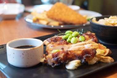 tavuk biftek sosu siyah plaka üzerinde fincan ile kapatın. Yeşil bezelye ve beyaz lahana, havuç ve restoranda mantarlı tavuk biftek üzerinde Japon deniz yosunu