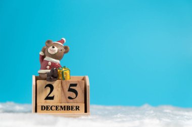 Kahverengi ahşap blok takvim üzerinde oturan bir Noel şapka Ayı beyaz yün ve mavi arka plan Christmas tarihi 25 Aralık olarak ayarlayın. Metin veya içerik için alan kopyalayın. 25/12 mutlu Noeller kavramı.